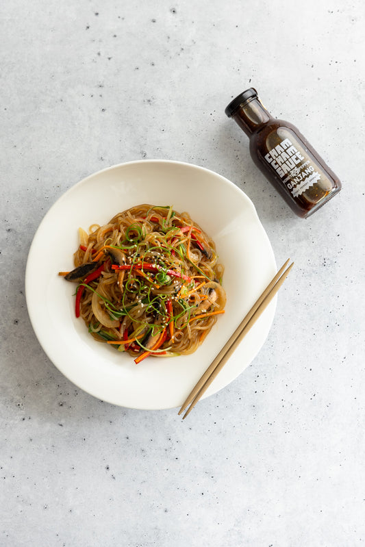 Bowl of Honey Pepper Japchae with bottle of Sauce